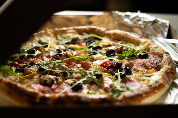 Pizza mit Oliven und Salamiwurst im Karton mit Lieferung nach Hause. Backen für Mittag- und Abendessen.