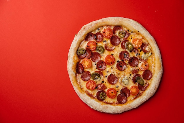 Pizza mit Räucherwurst Kirschtomaten getrocknete Chili Jalapenopfeffer und Mozzarella Roter Hintergrund Draufsicht Kopierbereich