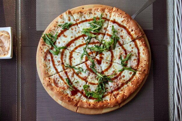 Pizza mit Rucola auf einer Holzplatte auf grauem Hintergrund auf der Sommerterrasse.