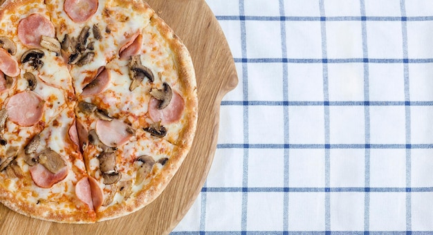 Pizza mit Schinken und Pilzen auf einem Holzbrett und blauer Serviette Draufsicht Foodphoto für Pizzeria-Menü
