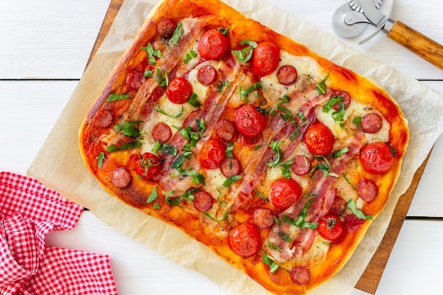 Pizza mit Speck, Wurst, Mozzarella, Tomaten und Basilikum. Italienische Küche. Rezept.