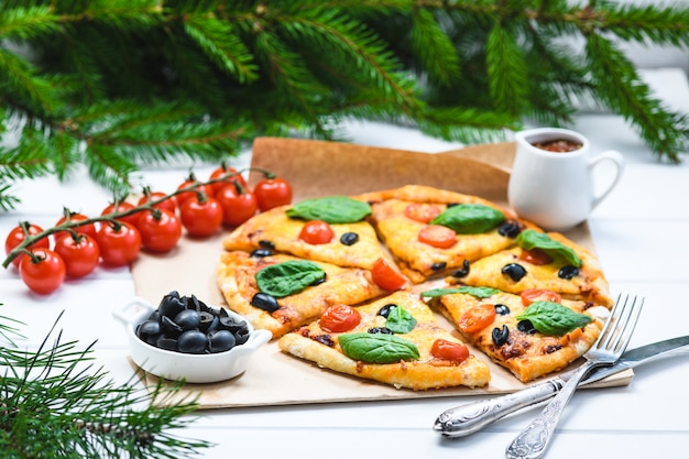 Pizza mit Tomaten und Spinat auf weißem Hintergrund und Weihnachtstannenzweigen