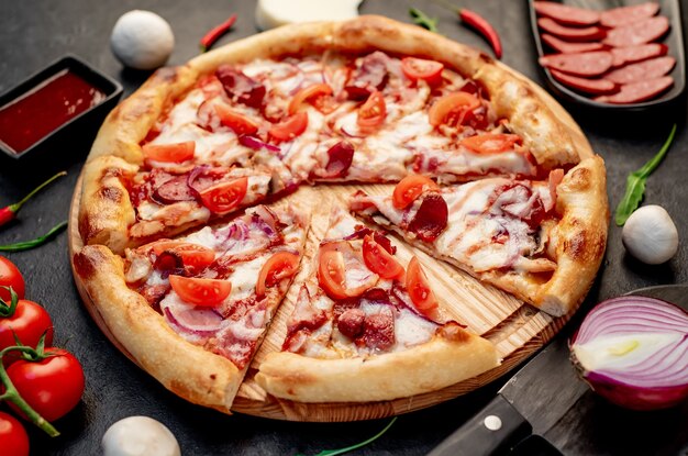 Pizza mit Würstchen, Champignons, Tomaten und Käse auf Steinhintergrund