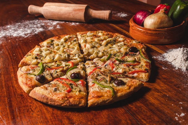 Pizza mitad vegetariana mitad palmito cortada en trozos sobre una mesa de madera.