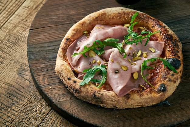 Pizza con mortadela, rúcula y pistachos sobre una tabla de madera. Cocina italiana