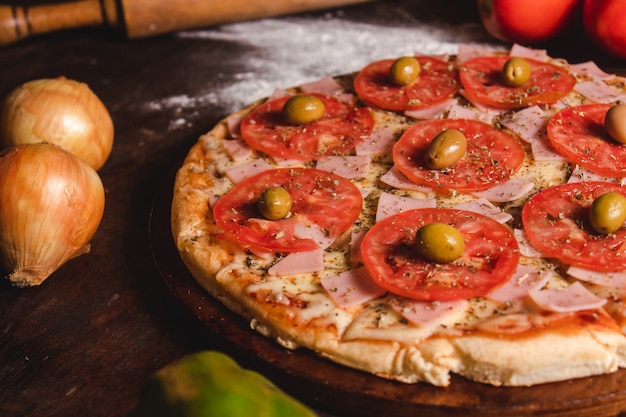 Una pizza con mucho queso, tomate, orégano y aceitunas en una mesa de madera.