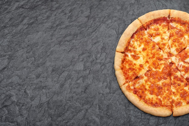 Pizza napolitana Margherita com tomate e queijo mussarela em fundo de ardósia preta.