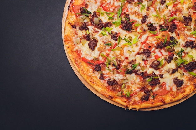 Pizza en papel sobre una tabla de madera. Pizza en primer plano de una mesa negra. Comida caliente saludable.