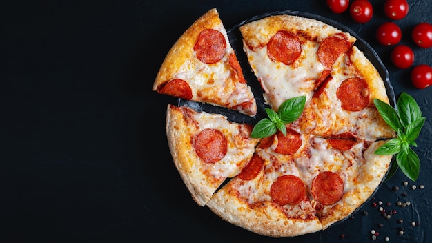 Pizza de pepperoni caliente e ingredientes para cocinar tomates albahaca sobre fondo de hormigón negro