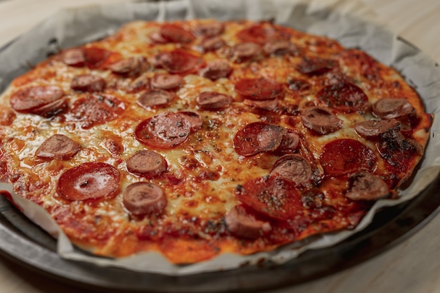 Pizza de pepperoni y salchicha casera en bandeja de metal con una servilleta negra en una mesa de madera