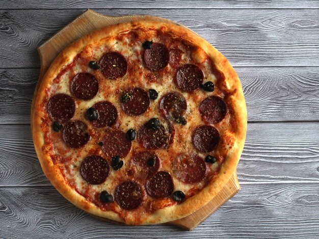 Pizza de pepperoni con sales y aceitunas sobre un fondo gris