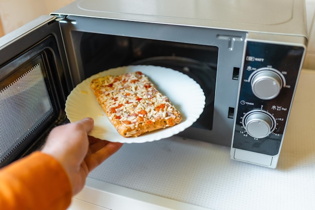 Pizza pequeña congelada sin cocer colocada en el microondas comida chatarra concepto de comida rápida vista lateral enfoque selectivo