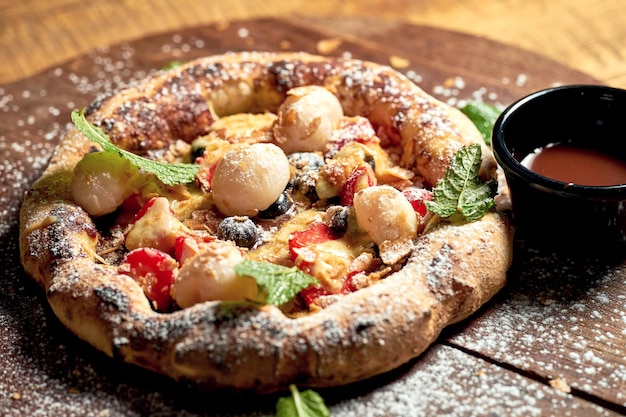 Pizza pequeña con fruta y helado en una tabla de madera sobre un fondo de madera Enfoque selectivo