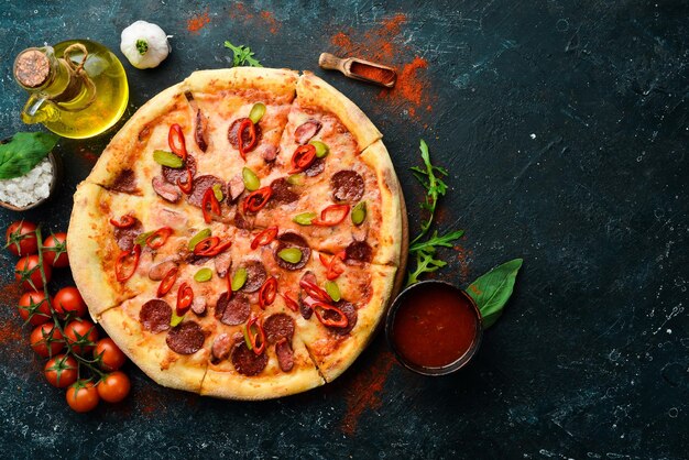 Pizza picante com salsichas e pimentas em um fundo de pedra preta Espaço livre para texto