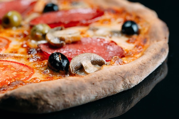 Pizza con primer plano de salchicha, champiñones, queso y pimienta.