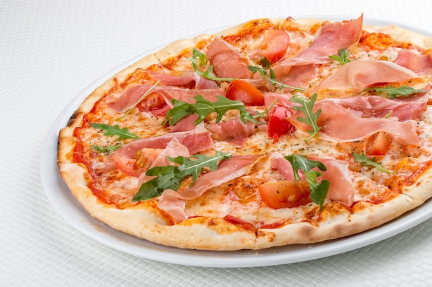 Pizza con prosciutto y rúcula sobre fondo blanco.