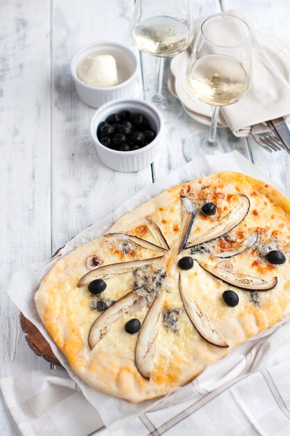 Pizza con queso brie y berenjenas sobre un fondo blanco de madera.