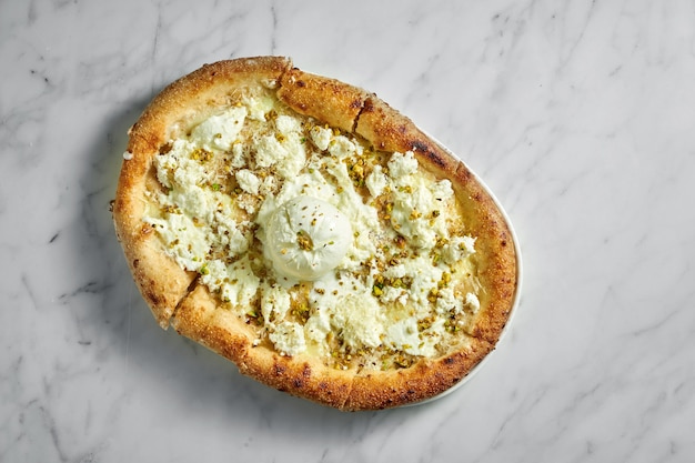 Pizza con queso crema, buratta, salsa de crema y pistacho en plato blanco sobre mármol blanco