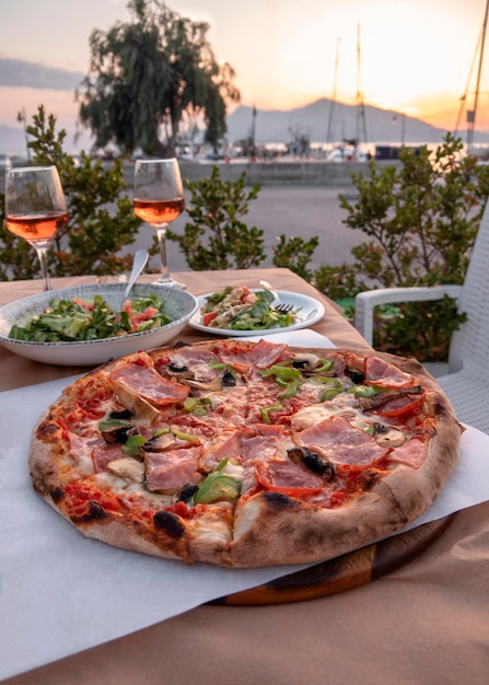 Pizza con queso, tocino, salami, champiñones y dos copas de vino en Grecia