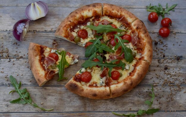 Pizza con queso y tomate sobre fondo de madera con cebolla. Se saca una rebanada de pizza.