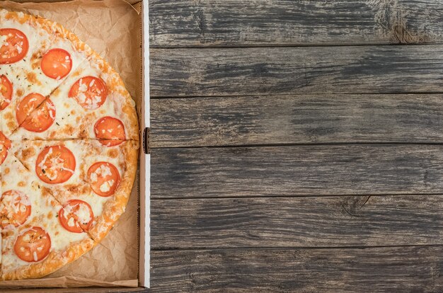 Pizza con queso y tomates en una caja con espacio de copia sobre un fondo de madera oscura.