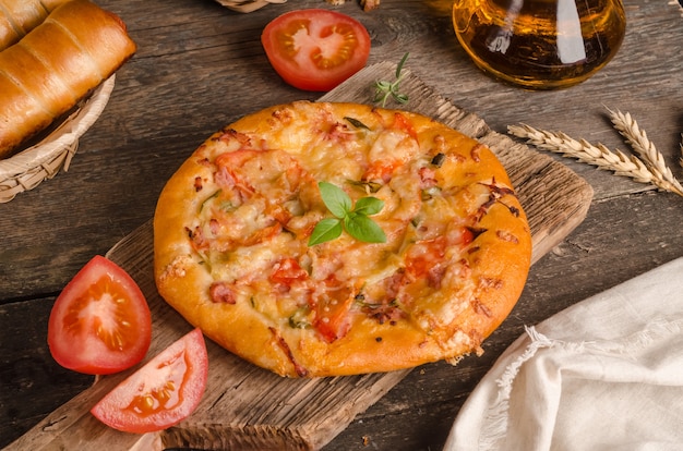 Pizza con queso y tomates sobre un fondo de madera con ingredientes, comida rápida