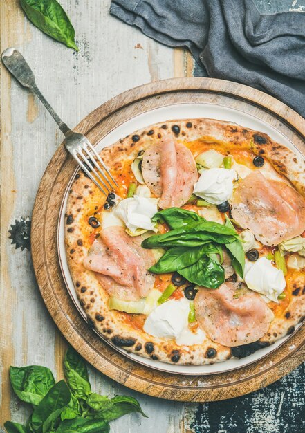 Pizza recém-assada com presunto, alcachofras, queijo e manjericão
