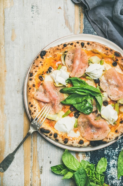 Pizza recién horneada con jamón, alcachofas, queso y hojas de albahaca