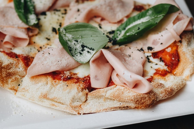 Pizza recién horneada con queso derretido hierbas italianas y salsa de tomate y albahaca fresca en un plato blanco sobre un fondo de cocina enfoque selectivo