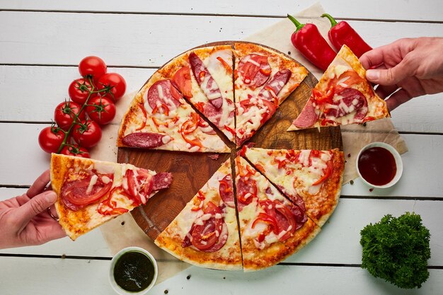 Pizza recién horneada con salchichas ahumadas pimiento rojo y tomates servidos sobre fondo de madera con salsa y hierbas Concepto de entrega de alimentos Menú del restaurante