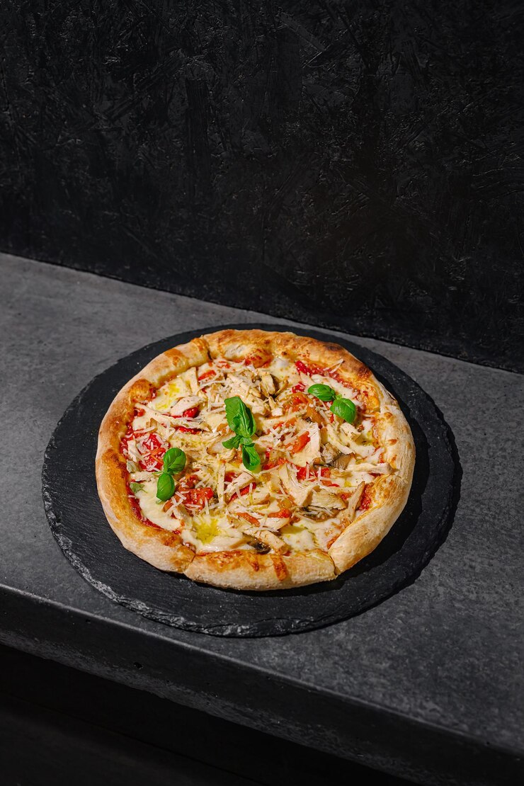 Pizza recién horneada con verduras y queso en una superficie de piedra oscura en un entorno contemporáneo