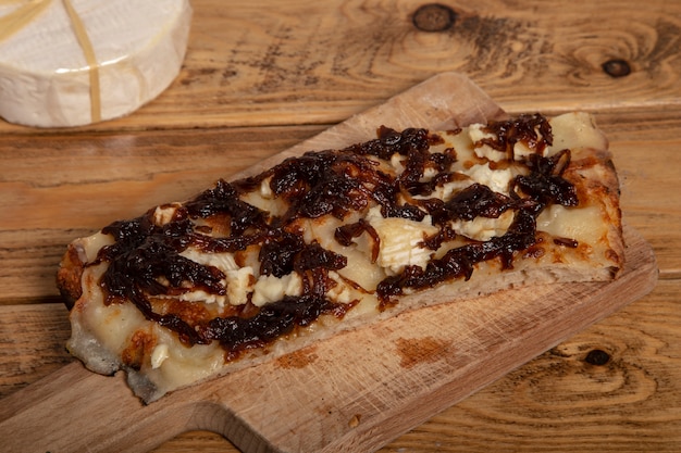 Pizza rectangular casera fresca con queso brie y cebolla caramelizada sobre una tabla para cortar madera.