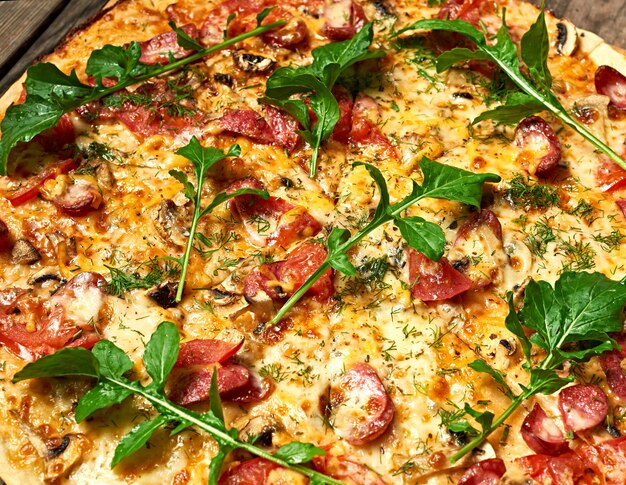 Pizza redonda al horno con salchichas ahumadas, champiñones, tomates, queso y hojas de rúcula