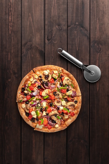 Pizza redonda fresca entera con carne de pollo, verduras, champiñones, queso y vista superior del cuchillo en una mesa de madera marrón. Sabrosa superficie de comida rápida en pizzería con espacio de copia