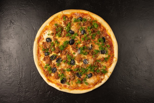 Pizza redonda quente recém-assada com atum, azeitonas, endro e queijo repousa sobre uma mesa de cozinha de pedra preta
