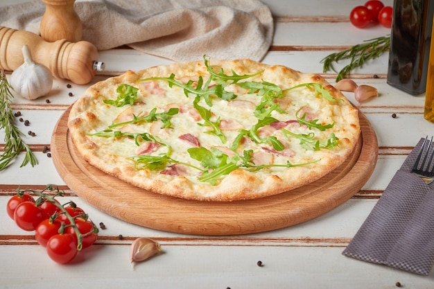 Pizza con rodajas, salsa y hierbas, madera blanca