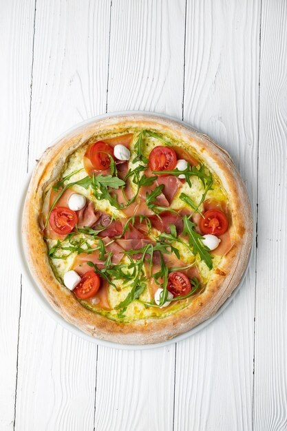 Una pizza con rúcula, mozzarella y rúcula sobre una mesa de madera blanca.