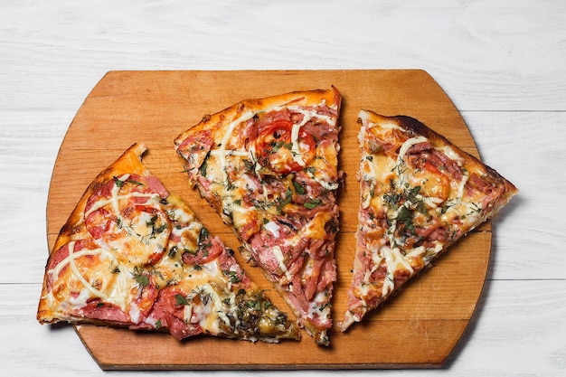 Pizza rústica italiana tres piezas en una bandeja de madera mesa de madera blanca con tomates y queso