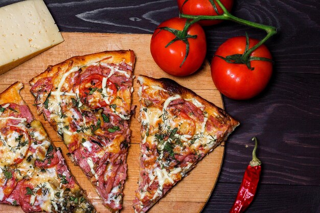 Pizza rústica italiana tres piezas en una bandeja de madera mesa de madera oscura con tomates, queso y chile