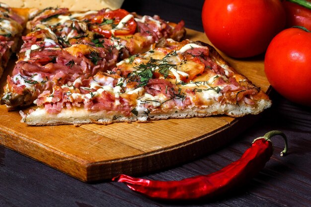 Pizza rústica italiana tres piezas en una bandeja de madera mesa de madera oscura con tomates, queso y chile
