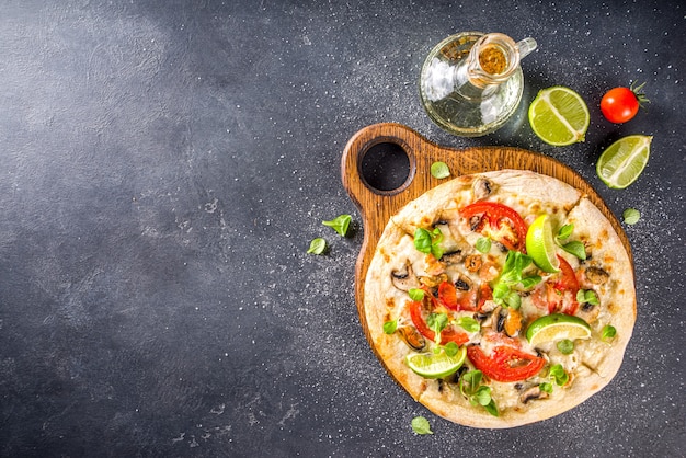 Pizza saborosa caseira com frutos do mar, tomates em uma mesa de pedra cinza