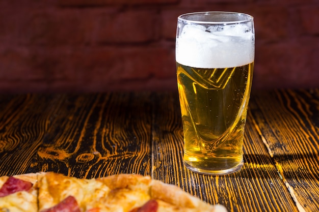 Pizza saborosa com recheios variados e queijos na mesa de madeira perto de um copo de cerveja