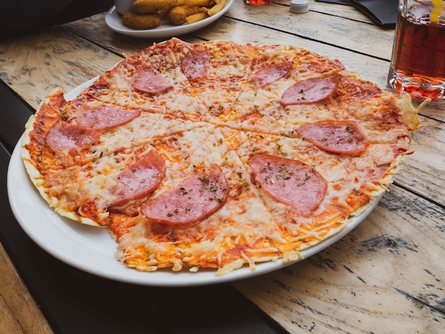 Pizza de salami entera en rodajas sobre una mesa de madera