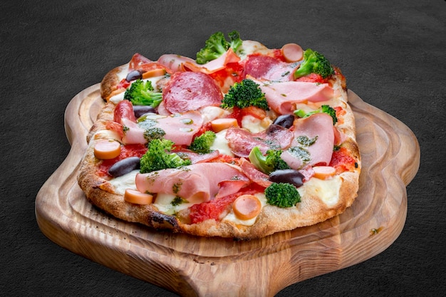 Pizza con salami, jamón, salchichas de Viena, aceitunas kalamata, brócoli, pelati, pesto, pizza romana rectangular sobre fondo oscuro.