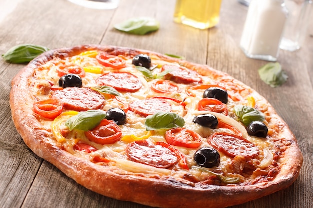 Pizza con salami y verduras sobre un fondo de madera vieja.