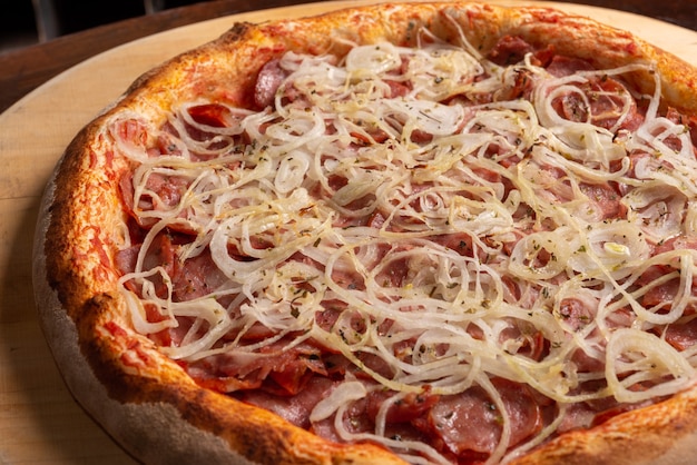 Pizza de salchicha de pepperoni con cebolla sobre una tabla de madera Pizza brasileña