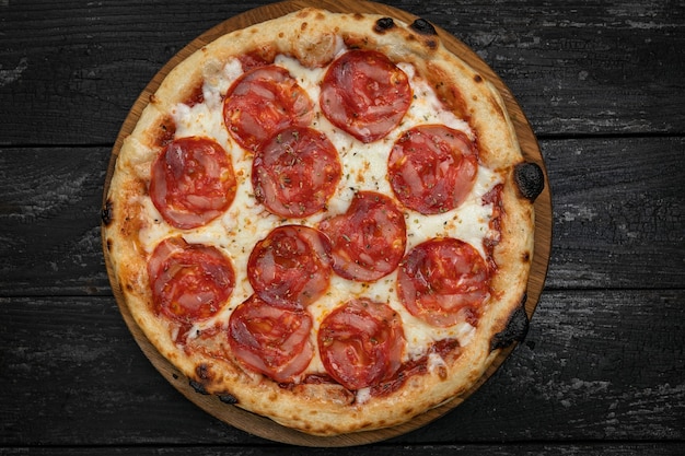 Pizza con salchicha de salami sobre una tabla de madera sobre una mesa oscura