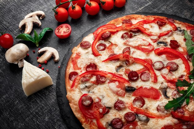 Pizza con salchichas ahumadas, queso, champiñones, tomates cherry, pimientos y verduras en una piedra.