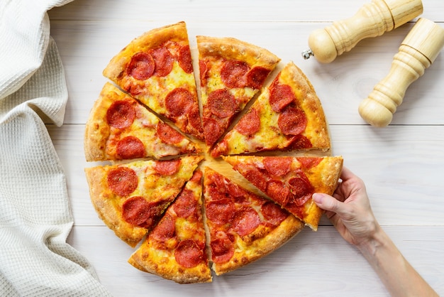 Pizza de salchichón en una mesa de madera clara. La mano toma un trozo de pizza.