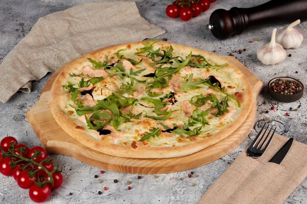 Foto pizza con salmón y rúcula sobre tabla de madera, fondo gris